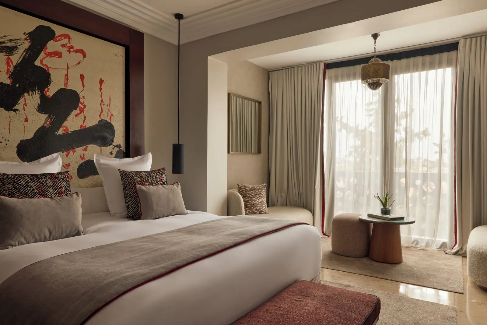 Junior Family Suite at Nobu Hotel Marrakech: a large bed under a calligraphy panel, with a small seating corner by sheer-curtained windows