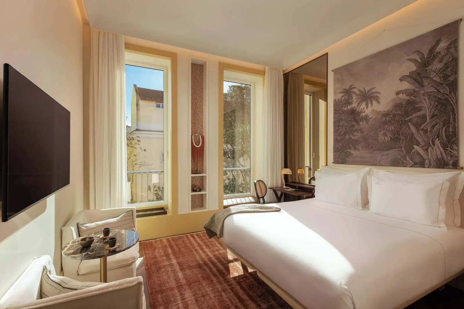 Capelo King at The Ivens: the bed under a palm tapestry, an armchair and two tall windows