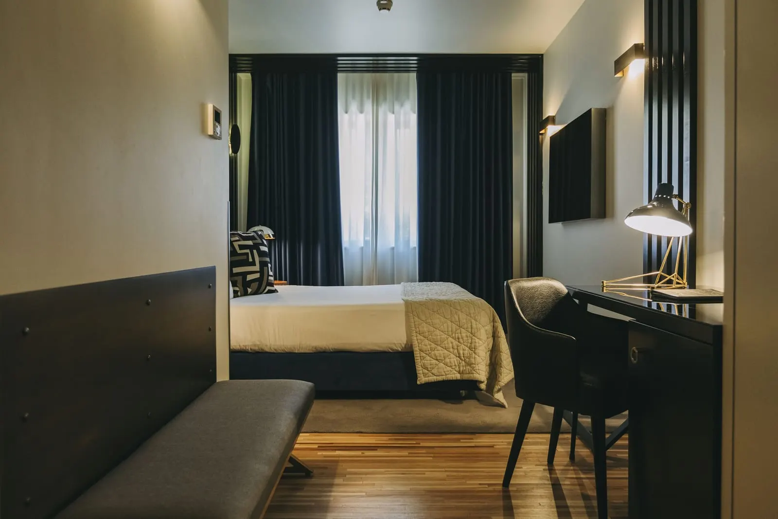 Executive Room at Torel Avantgarde: the bed by a curtained window, with a desk, a lamp and a bench
