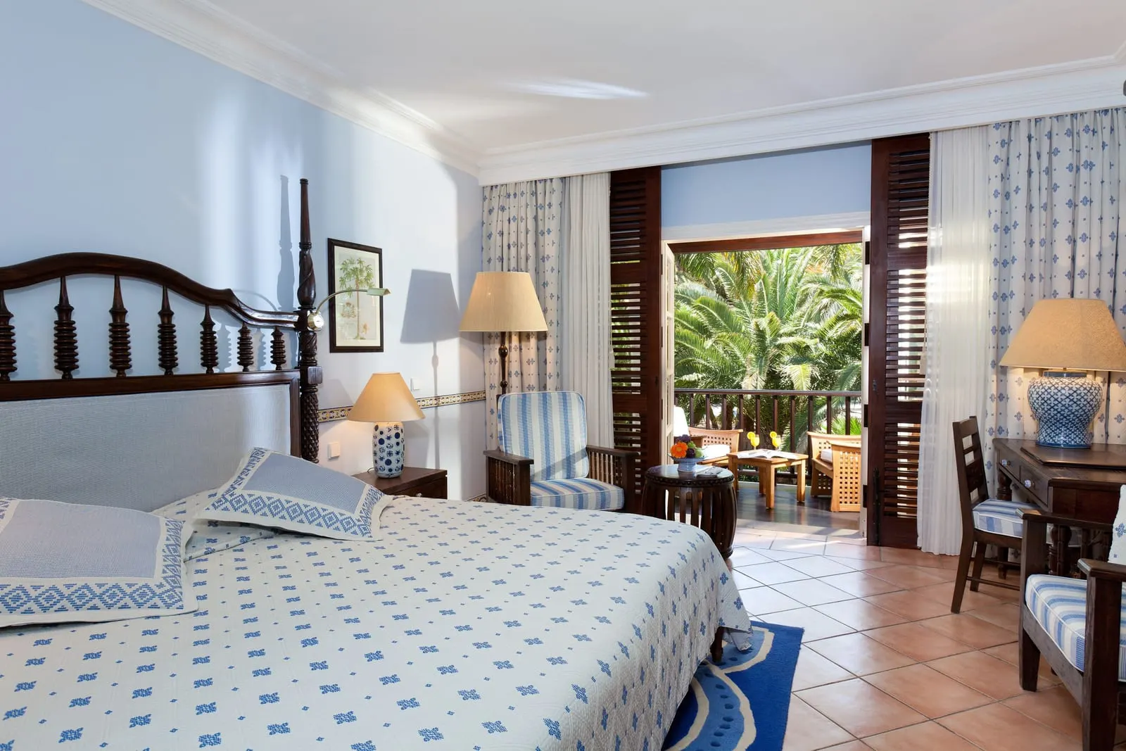 Twin Room at Seaside Grand Hotel Residencia: a double bed with a dark carved headboard, a striped armchair and a desk, with shuttered doors open to a balcony