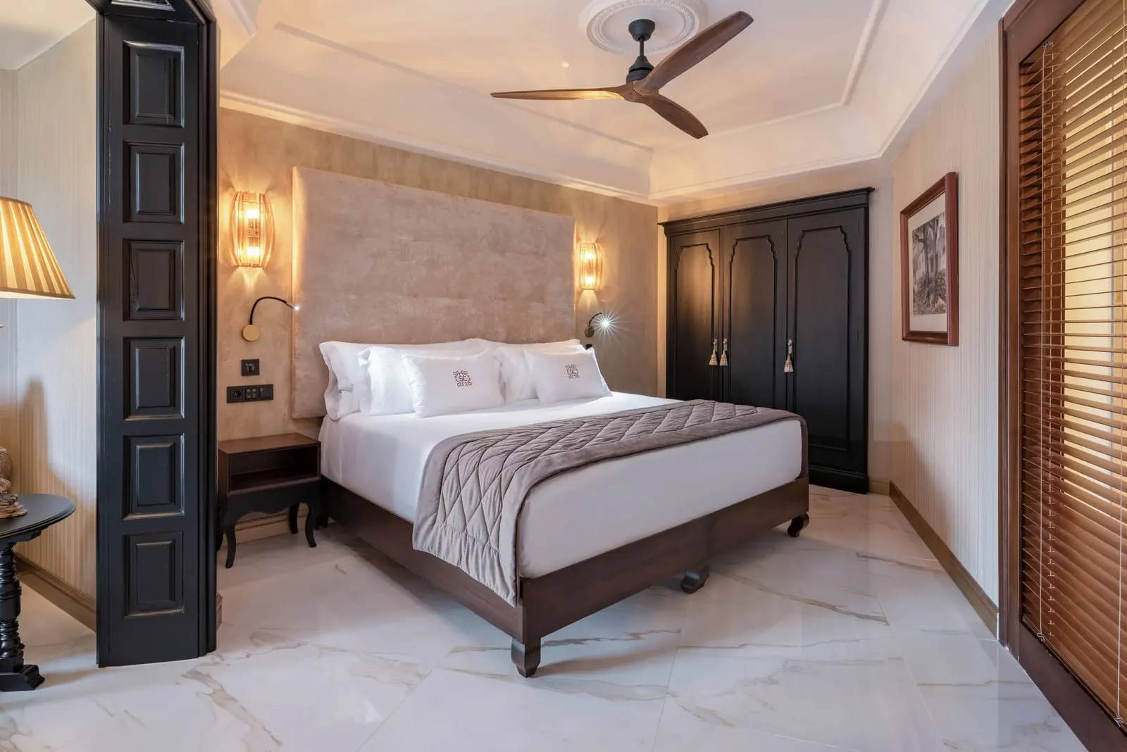 Suite at Santa Catalina, a Royal Hideaway Hotel: a double bed with a padded headboard and wall lamps, a dark wooden wardrobe and a ceiling fan over a marble floor