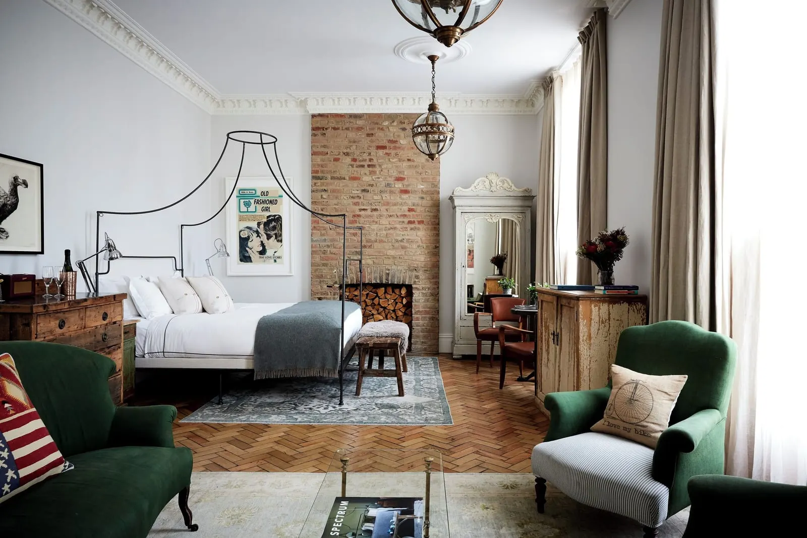 Grand Suite at Artist Residence London: the four-poster bed, green velvet armchairs, a brick chimney breast and tall windows