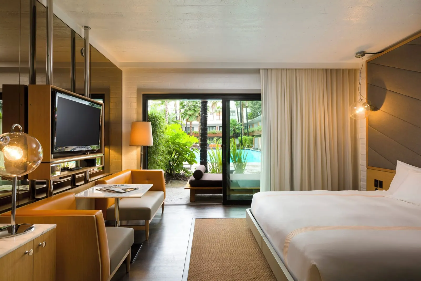 Cabana Poolside King at The Hollywood Roosevelt: a bed and leather banquette beside a swivel television, with sliding glass doors onto a patio and the pool beyond