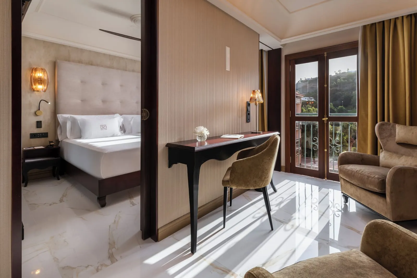 Junior Suite at Santa Catalina, a Royal Hideaway Hotel: a seating area with two velvet armchairs and a writing desk by glazed balcony doors, with the bedroom through an open sliding door
