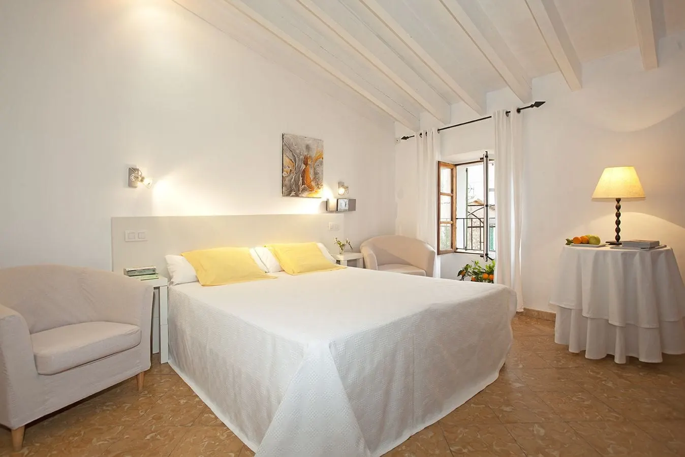Habitación con vistas al pueblo at Fornalutx Petit Hotel: a double bed with yellow cushions under white ceiling beams, two armchairs and an open shuttered window