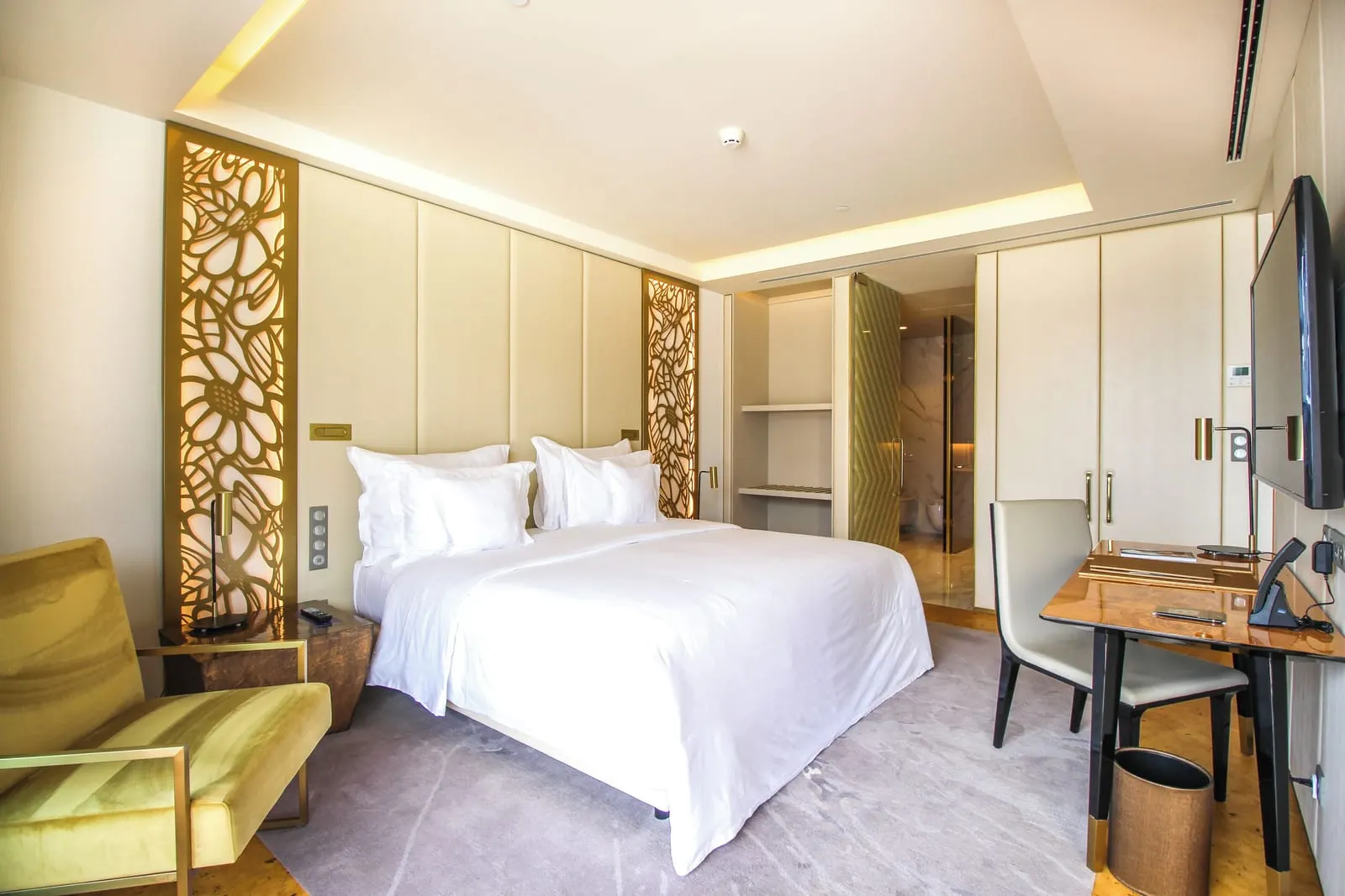 Bay Suite im Savoy Palace: ein Kingsize-Bett zwischen goldenen Gitterpaneelen, ein Samtsessel, ein Schreibtisch und ein Wandfernseher