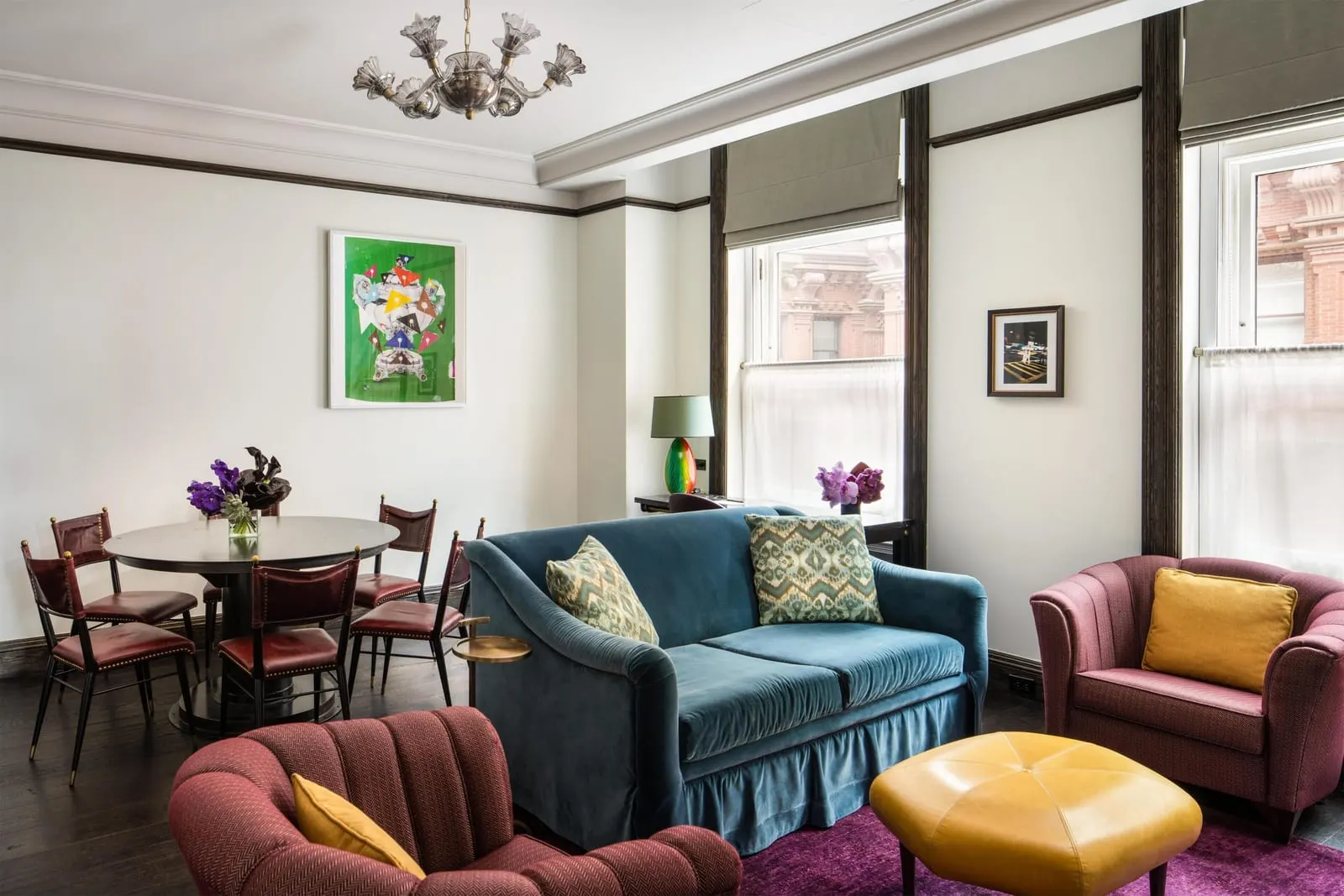 Deluxe Corner Suite at The Beekman: a living and dining room with a blue velvet sofa, burgundy armchairs, a leather ottoman and a round dining table with leather chairs