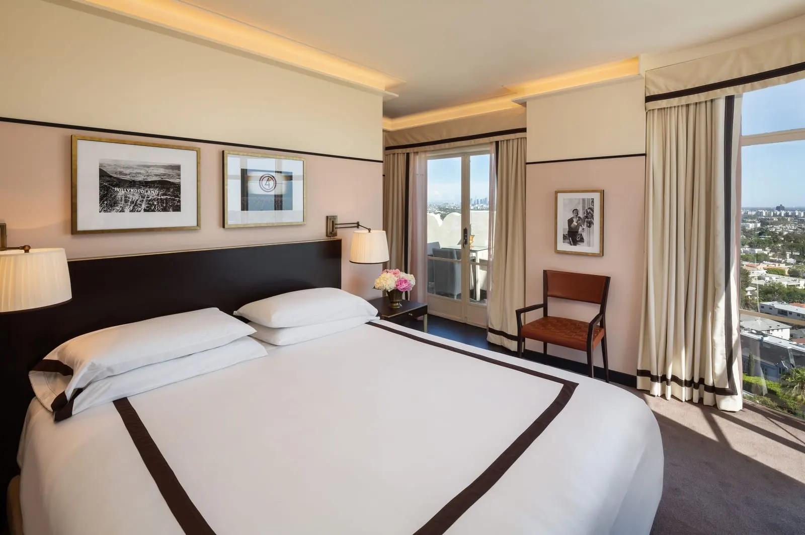 Studio Suite at Sunset Tower Hotel: a king bed with a dark headboard and framed prints, a leather chair and French doors beside a tall corner window
