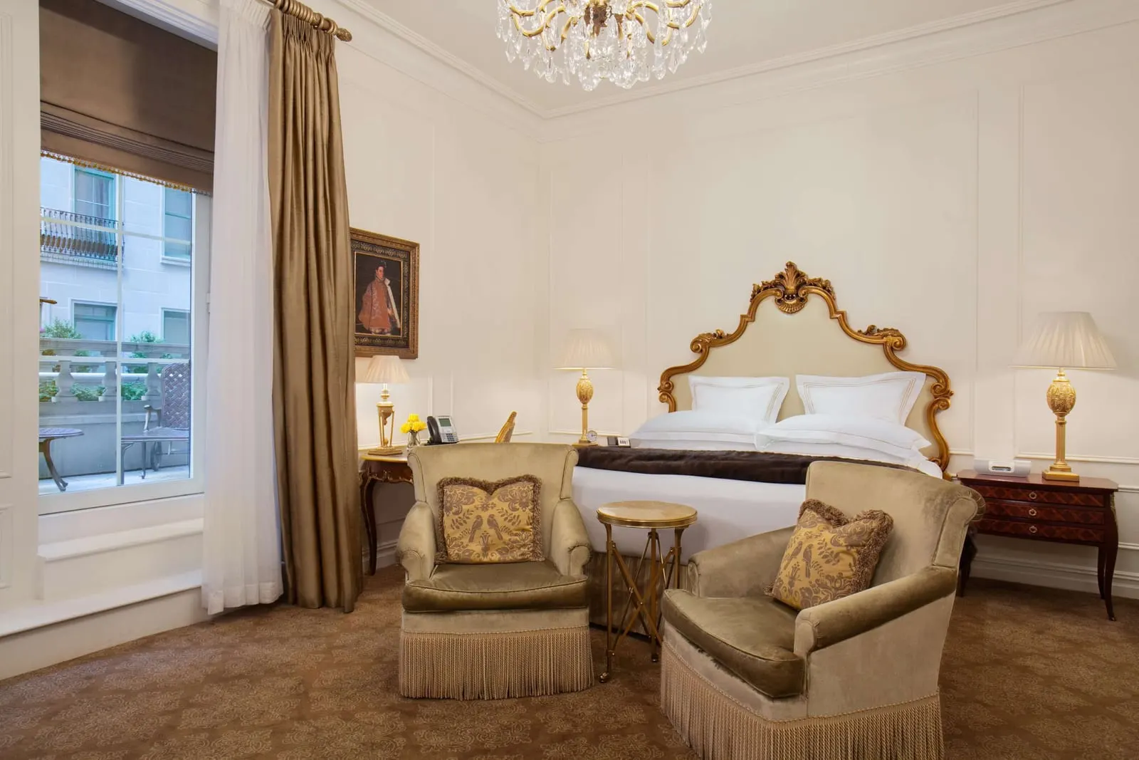 Terrace Room King at The Plaza: a king bed with a gilded headboard, two velvet armchairs and a desk, with a tall window onto a stone terrace with a table and chair