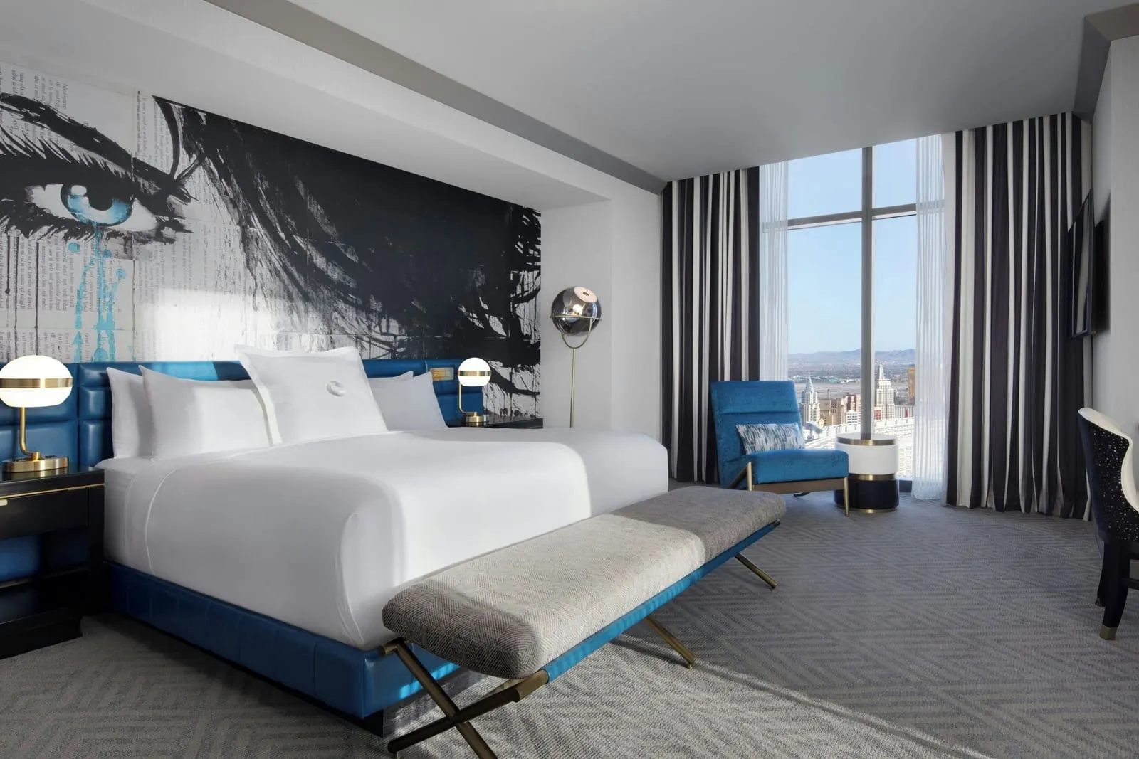 Two Bedroom City Suite at The Cosmopolitan of Las Vegas: a king bedroom with a large painted mural of a woman's eye above a blue headboard, a blue armchair and a full-height window