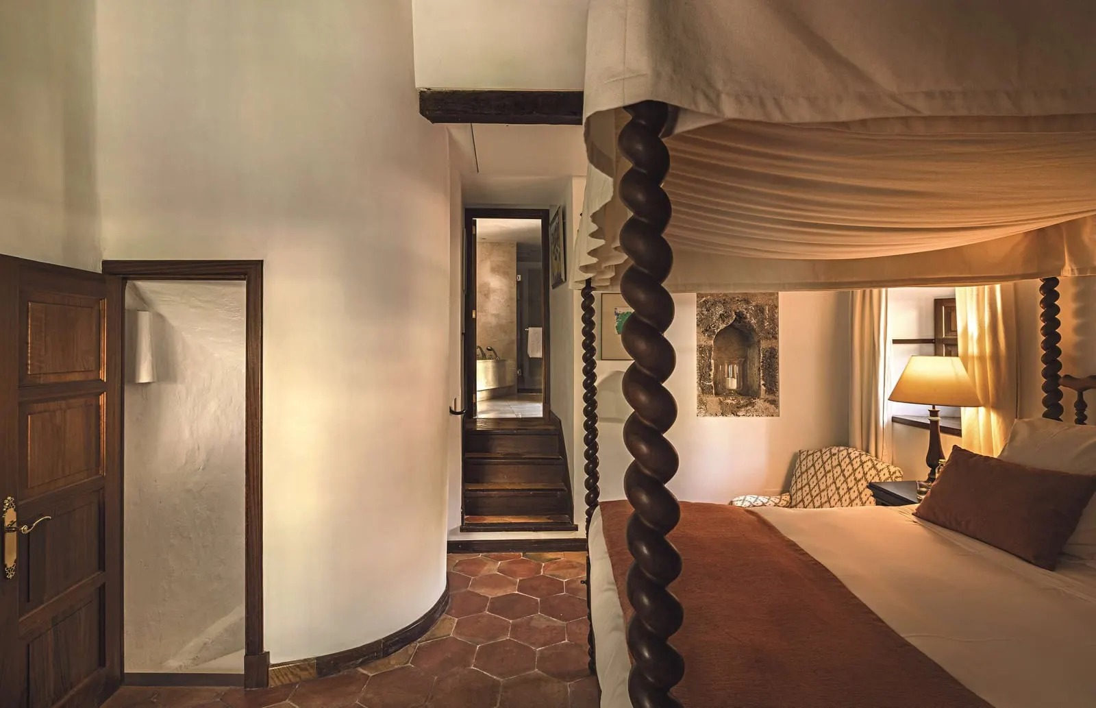 Tower Suite at Belmond La Residencia: a four-poster bed with a draped canopy beside a curved white wall, with a short flight of steps leading to a doorway beyond
