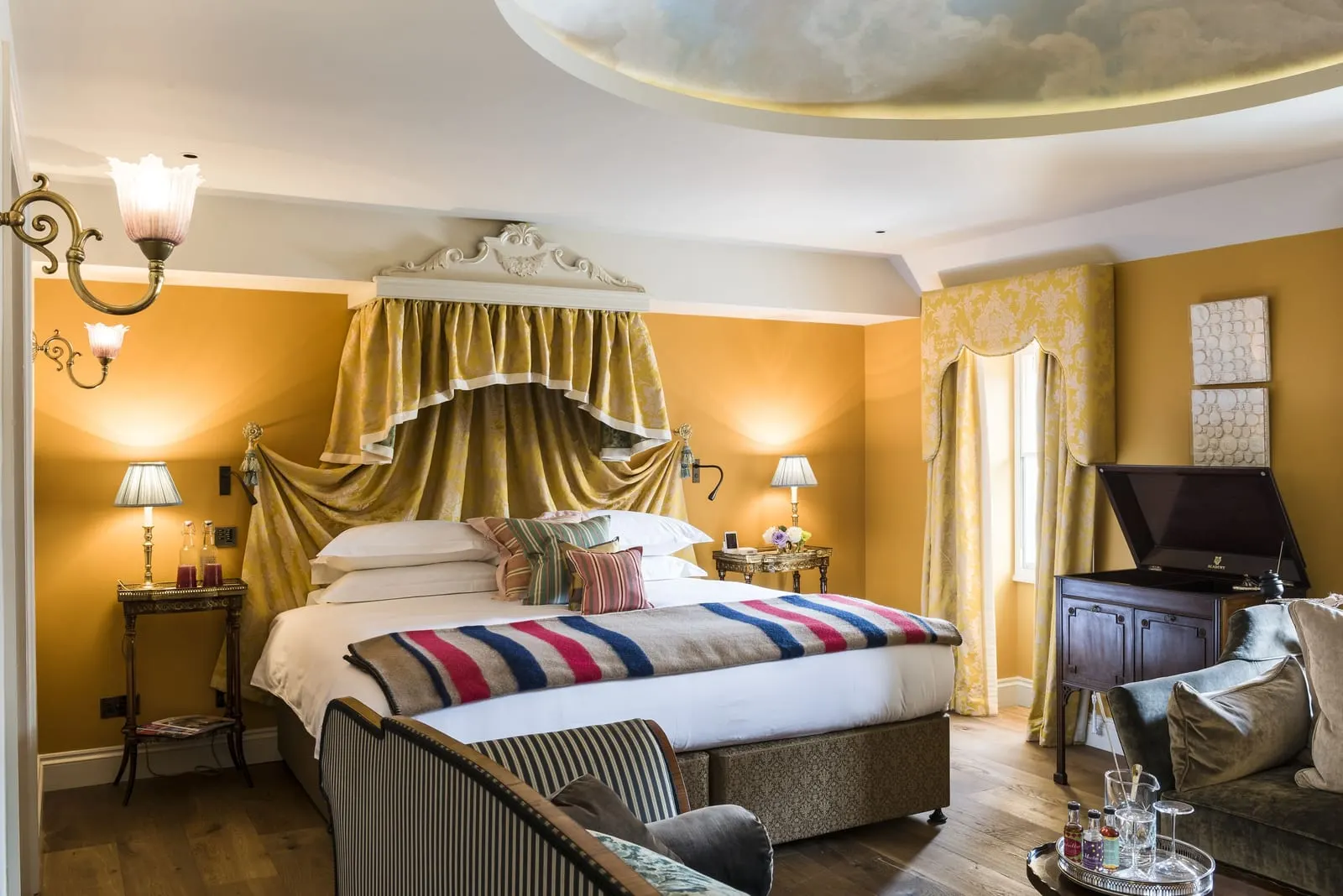 Lear's Loft at The Zetter Marylebone: a canopied bed against golden walls, with a striped blanket and armchairs