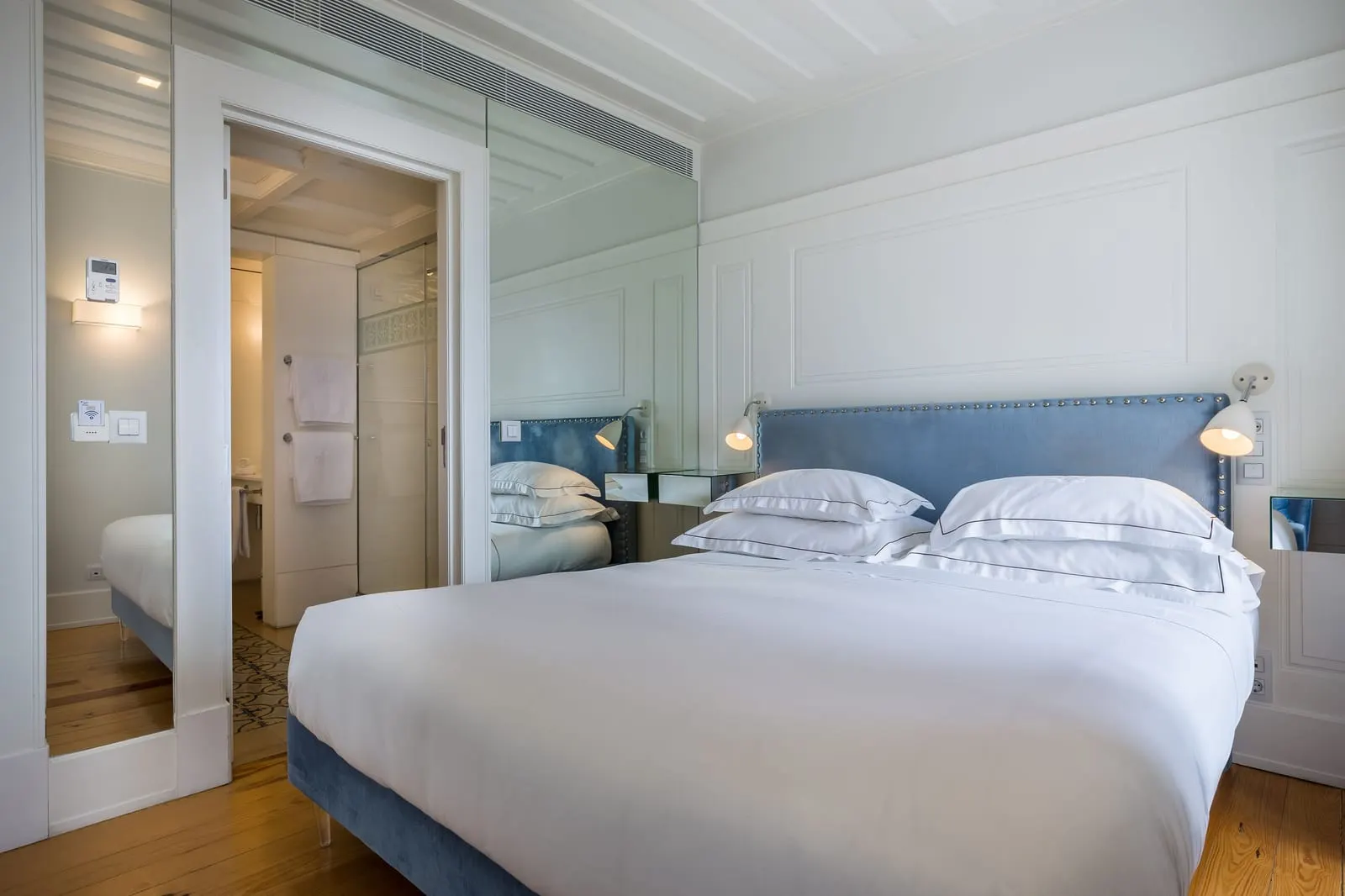Classic River Bedroom at Santiago de Alfama: the double bed with a blue headboard, a mirrored wall and the bathroom door
