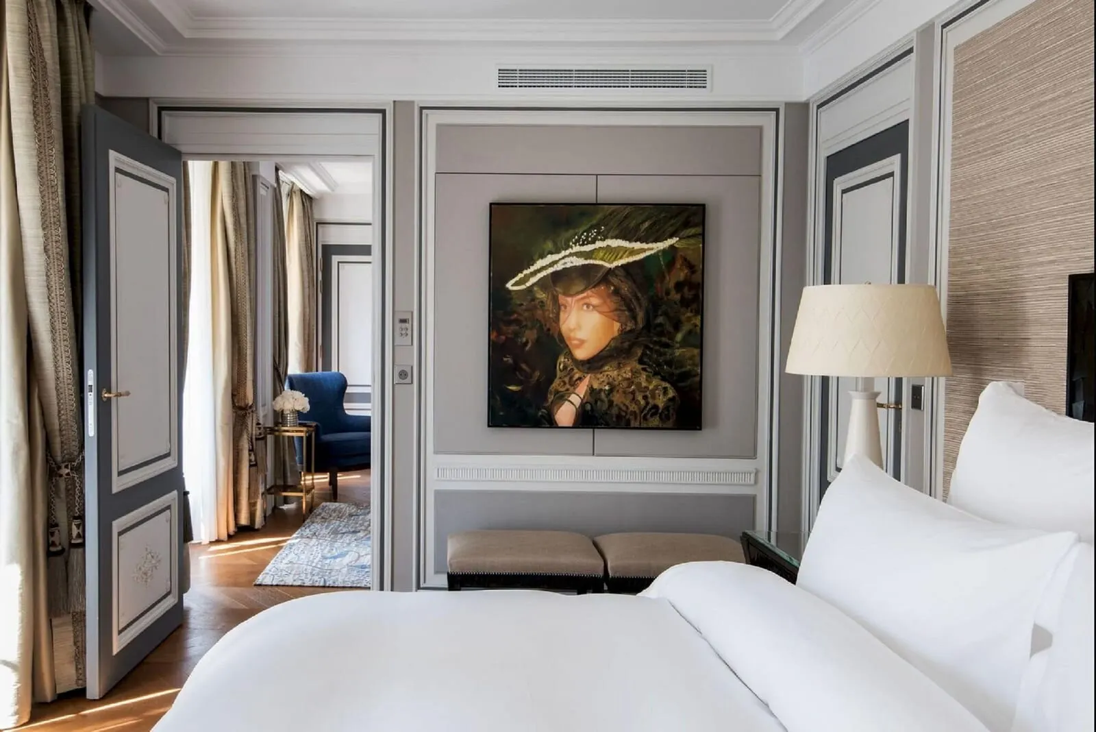 Deluxe Suite at Hôtel de Crillon, A Rosewood Hotel: the bedroom, with a large portrait above a pair of stools and an open door through to the lounge and its blue armchair