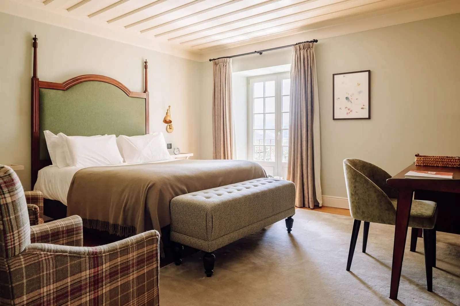Premium Manor House Accommodation at Quinta Nova: a bed with a green headboard, a tartan armchair, a desk and glazed doors