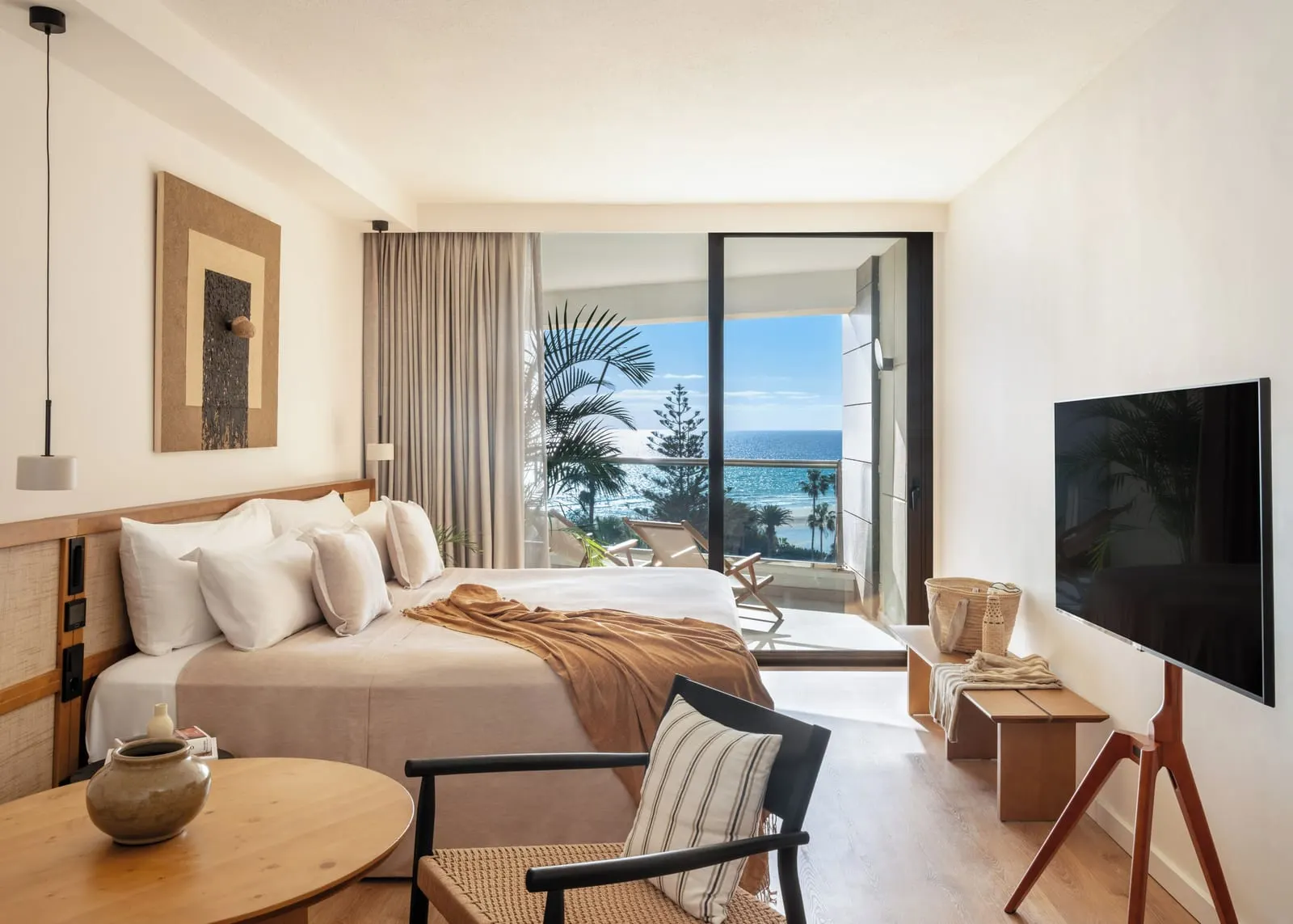 Premium Room Ocean Front at Paradisus by Meliá Fuerteventura: a king-size bed, a round table and a television on a stand, with a glass door to a terrace and the sea beyond