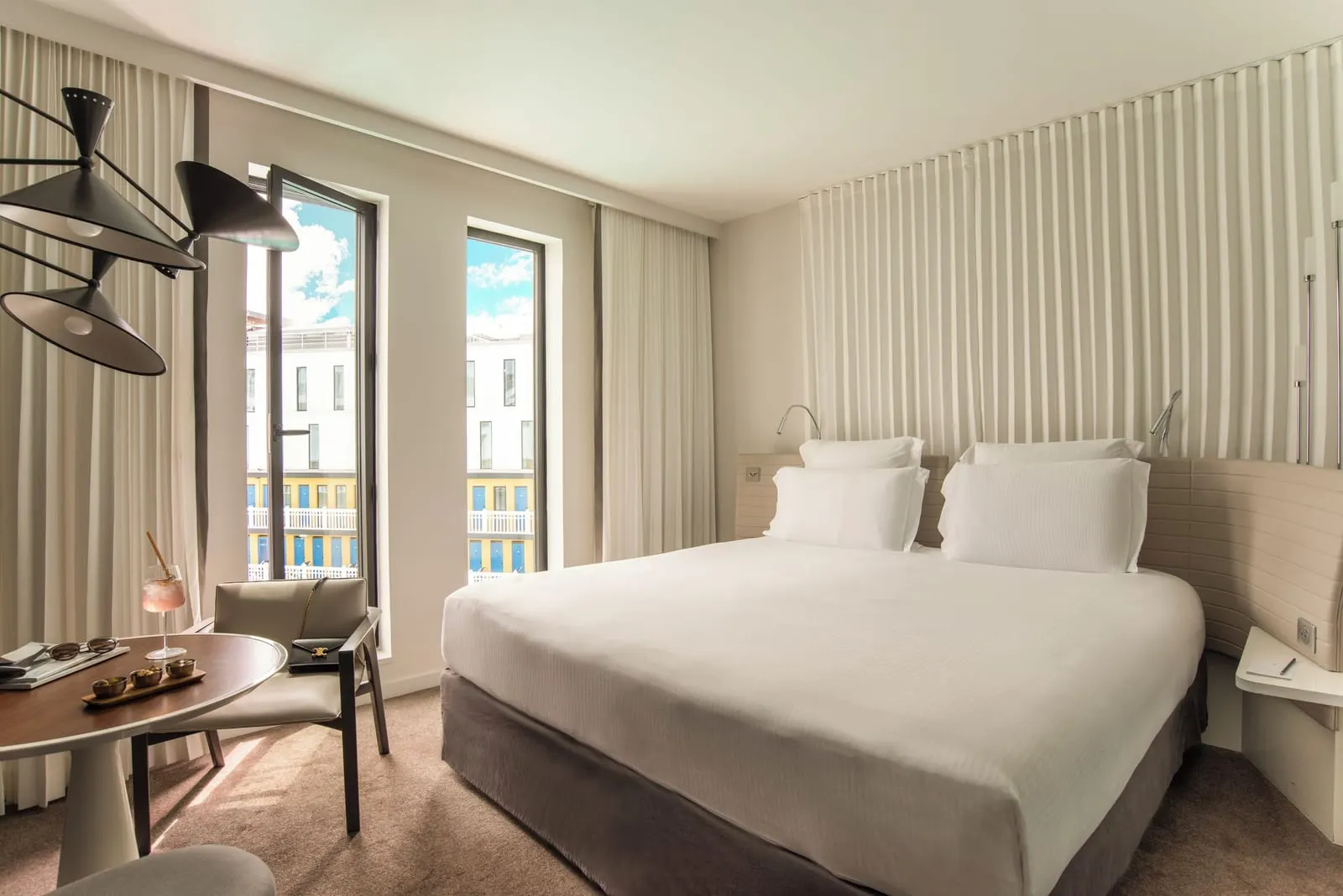 Superior Room at Hôtel Molitor Paris: a queen-size bed against a pleated curtain wall, a round table with an armchair and two tall windows, one of them open