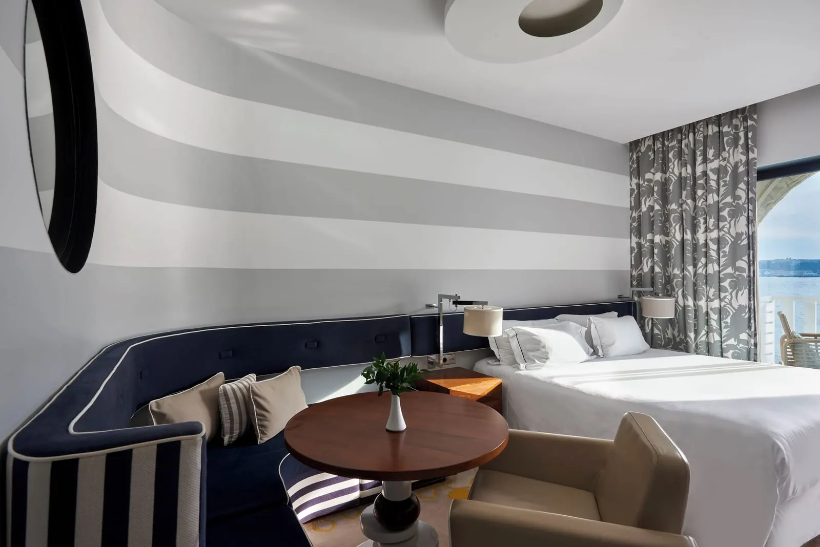 Exclusive Room at Monte-Carlo Beach: the bed, a navy banquette around a round table and grey striped walls
