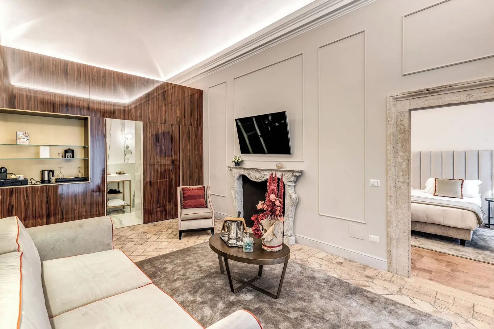 Deluxe Suite at Eitch Borromini Palazzo Pamphilj: a sofa and armchair by a stone fireplace, with the bedroom through the doorway