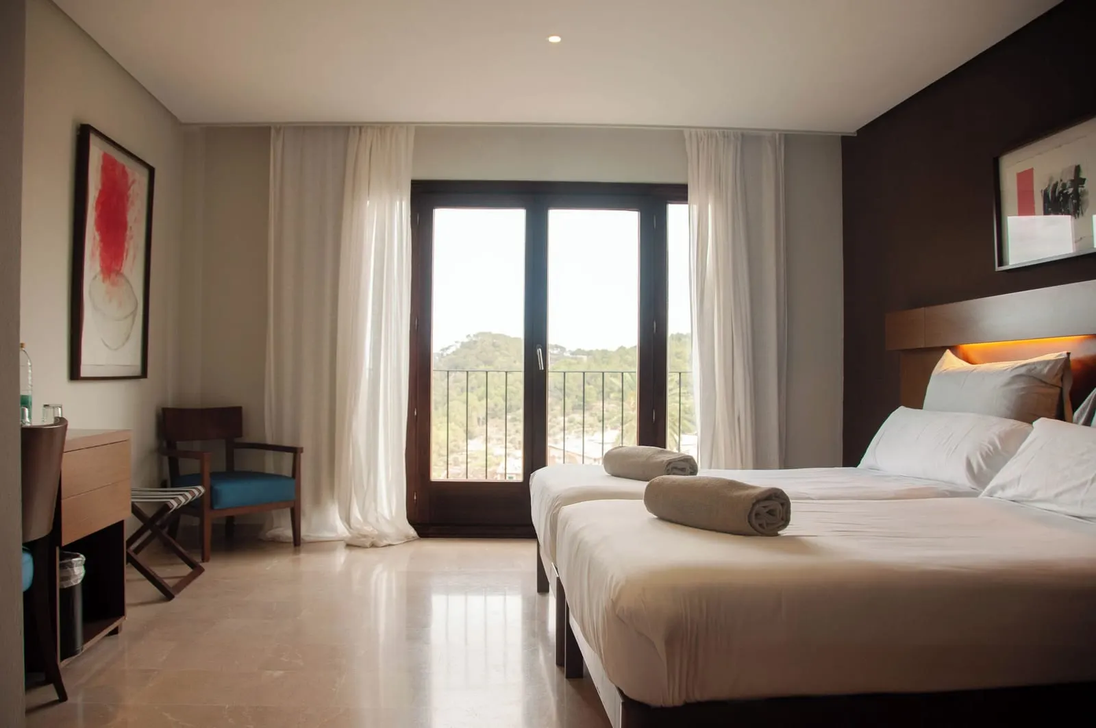 Scenic Window at Maristel Hotel & Spa: two beds with rolled towels, a desk and an armchair, and tall balcony doors onto wooded hills