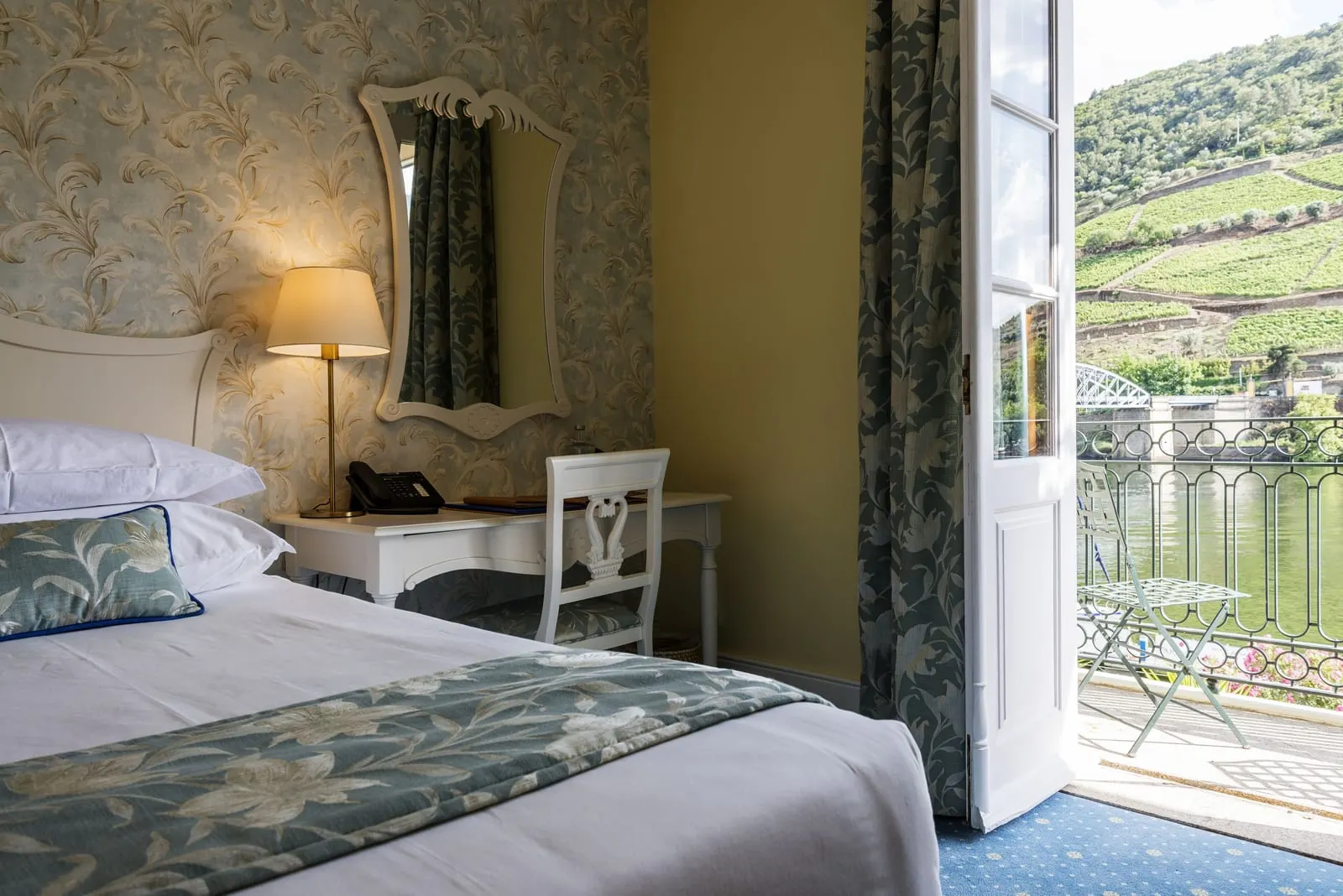 Standard Room at The Vintage House: the bed, a small desk and a door open to a balcony above the Douro