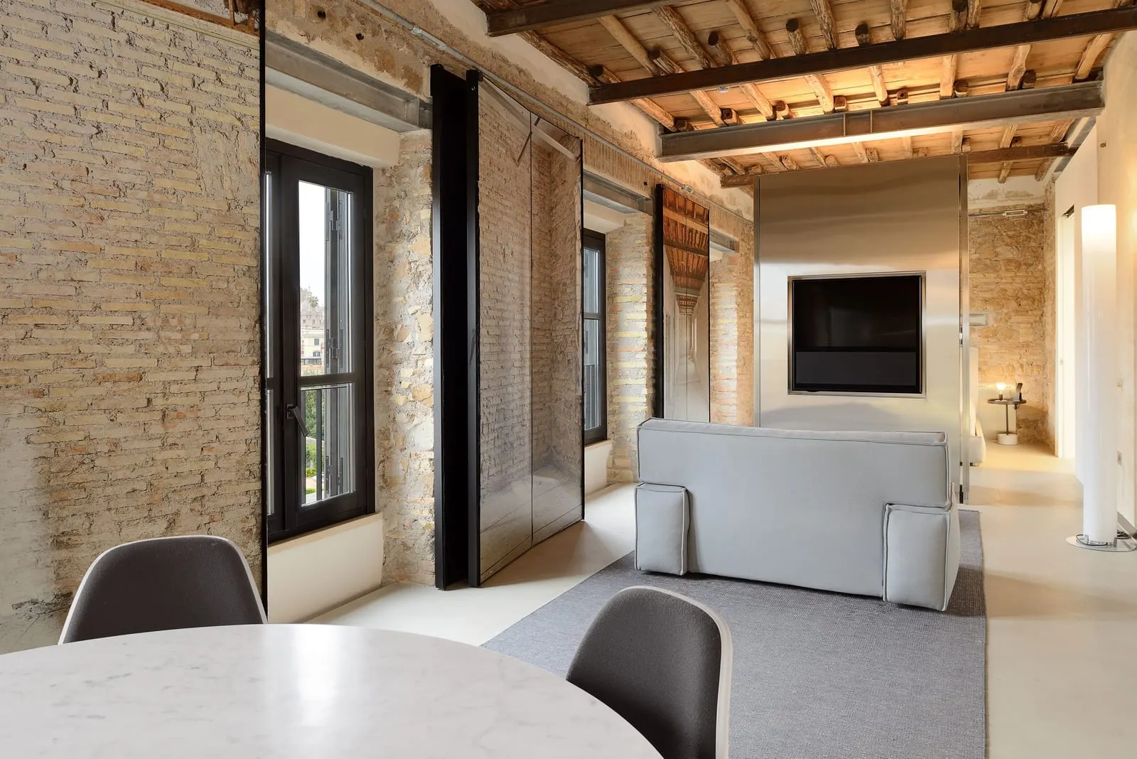 Suite Apartment Single at Rhinoceros Roma: a dining table and a grey sofa facing a TV, brick walls and a beamed ceiling