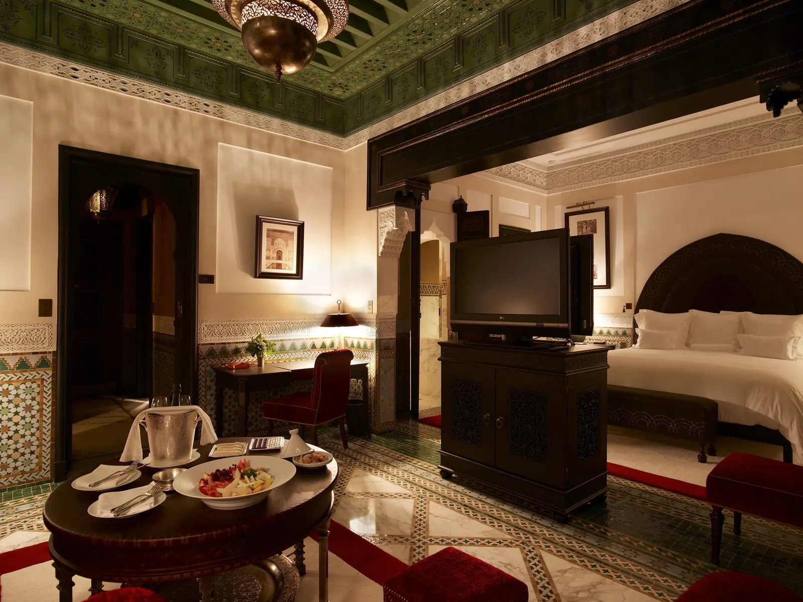 Agdal Suite at La Mamounia: a bedroom under a painted green ceiling and brass lantern, with a breakfast table set by the bed