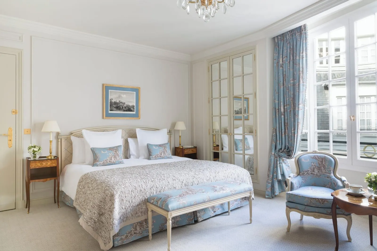 Executive Room at Le Bristol Paris: a king bed with blue toile cushions and a matching bench, a toile armchair and a small round table by the tall window, and mirrored wardrobe doors