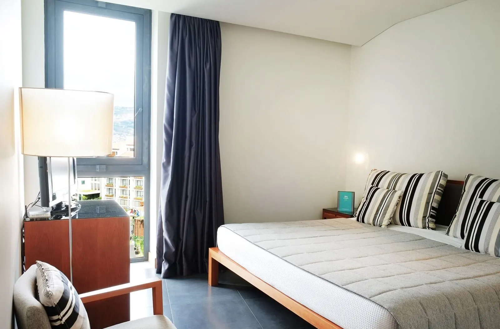 VidaMar Resort Hotel Madeira Master Suite Sea View：大きなベッド、ストライプ柄のクッション、アームチェア、背の高い窓がある寝室