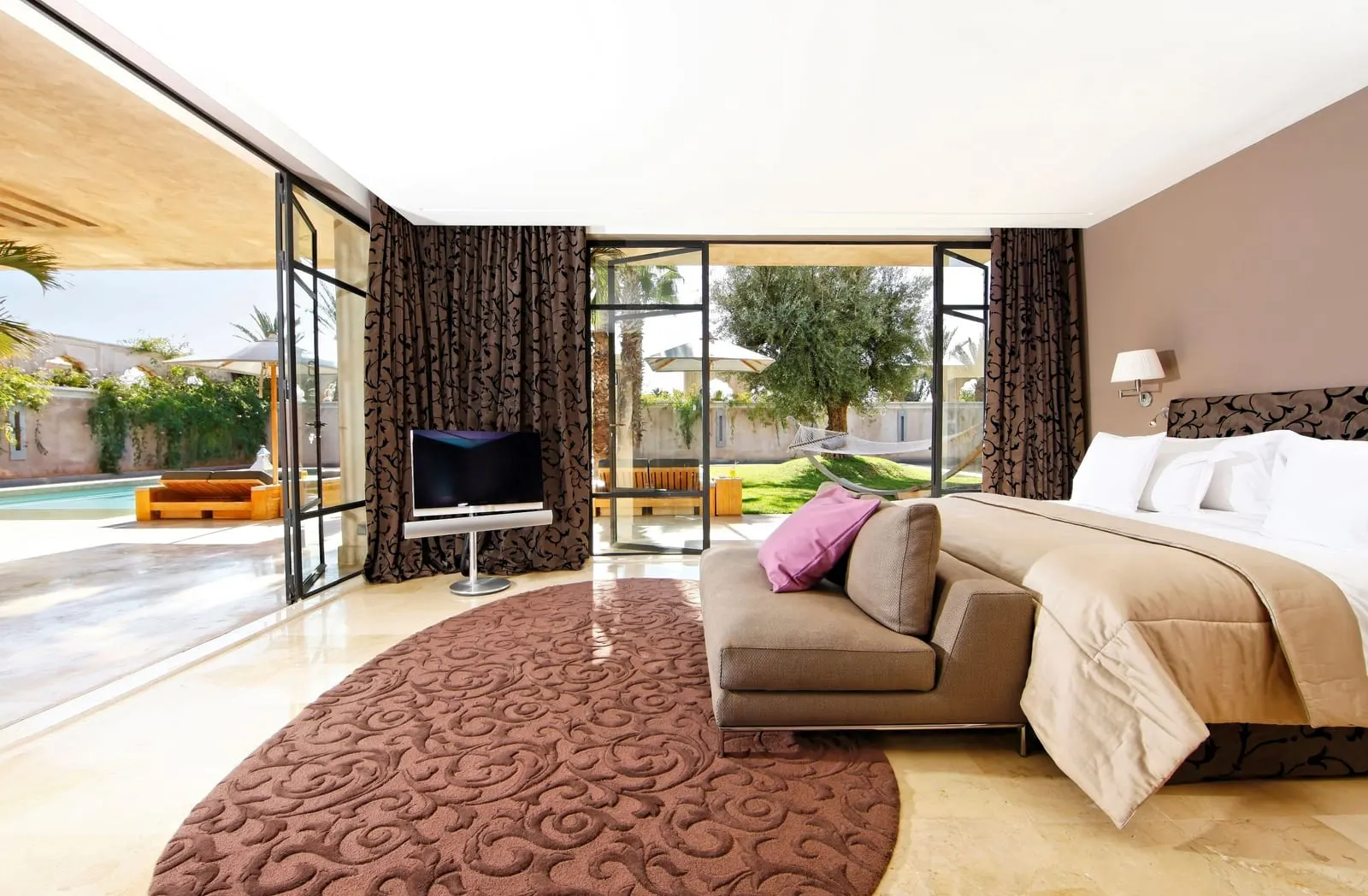 Villa Namaskar at Palais Namaskar: a bedroom with a sofa at the foot of the bed and glass doors onto the garden and pool