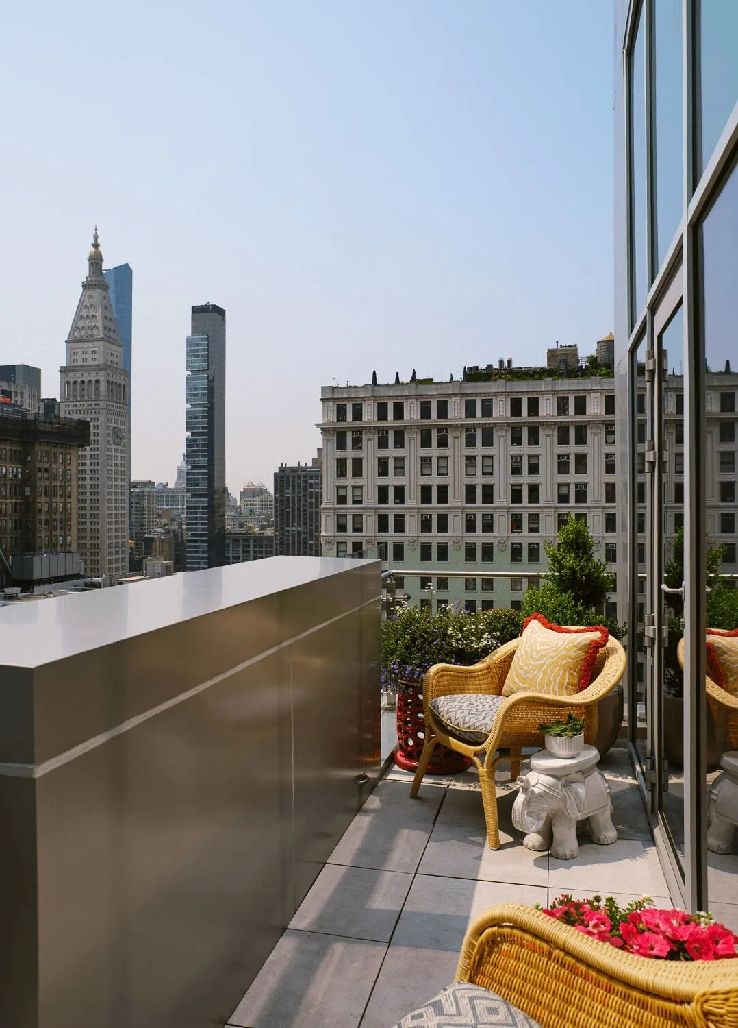 One Bedroom Terrace Suite at The Fifth Avenue Hotel: a terrace with wicker armchairs, an elephant shaped side table and planters, behind a metal parapet