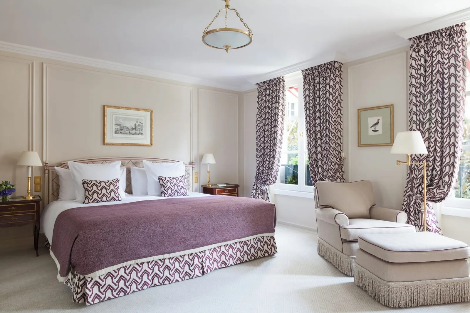 Deluxe Room with garden view at Le Bristol Paris: a bed with a plum throw, an armchair and footstool by the windows and a brass floor lamp, against cream panelled walls