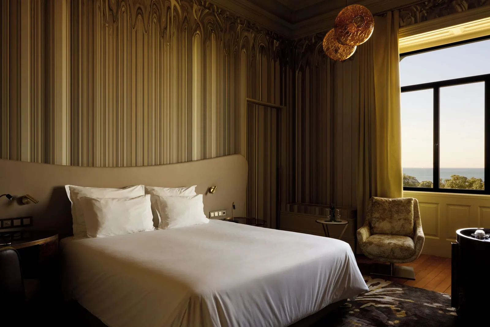 Manor House Ocean Front Room at Vila Foz: the bed, an armchair and a tall window with the sea on the horizon