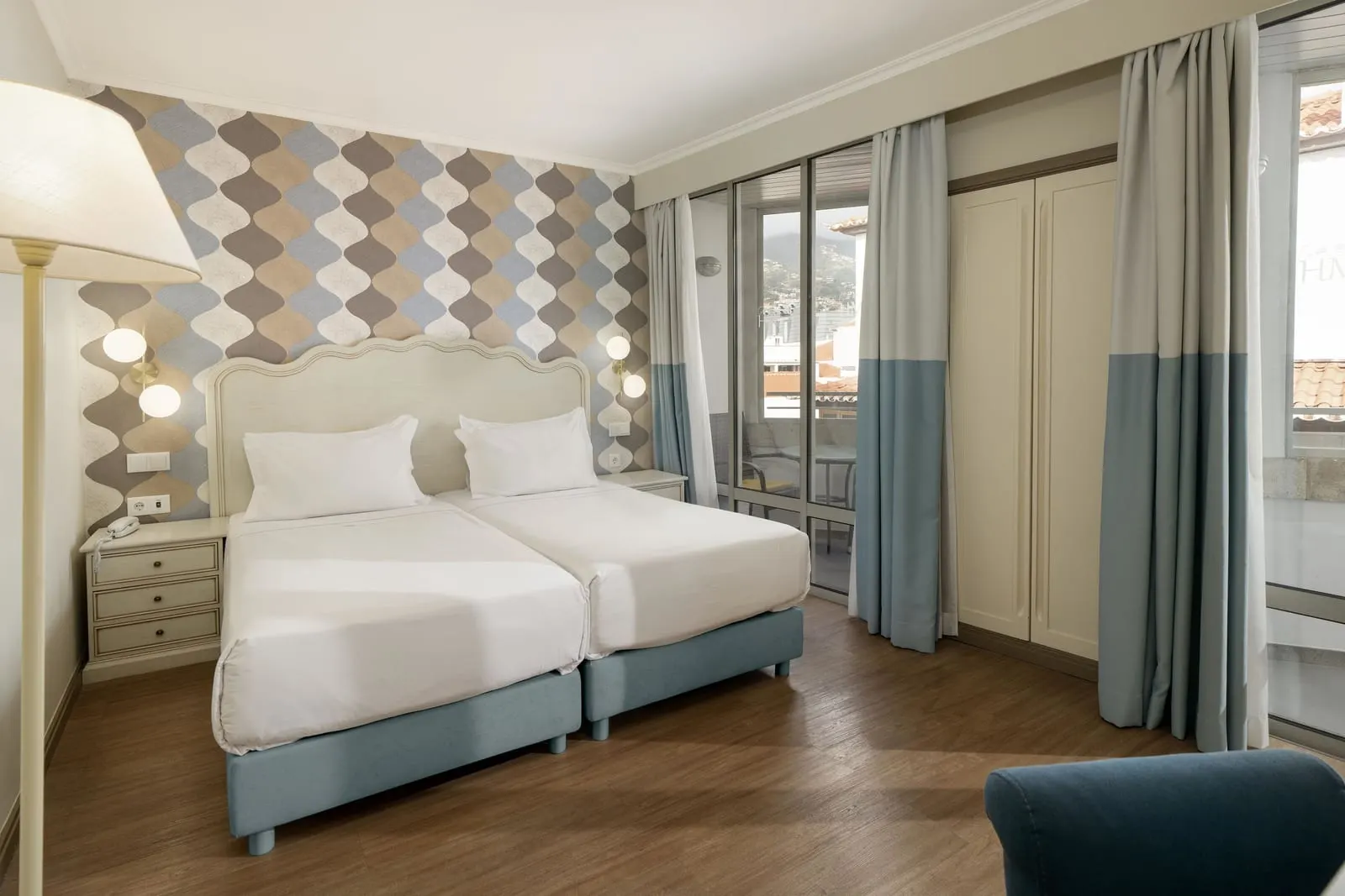 Superior Room with Balcony im Hotel Madeira: zwei Einzelbetten vor einer gemusterten Akzentwand, mit raumhohen Glastüren zum Balkon