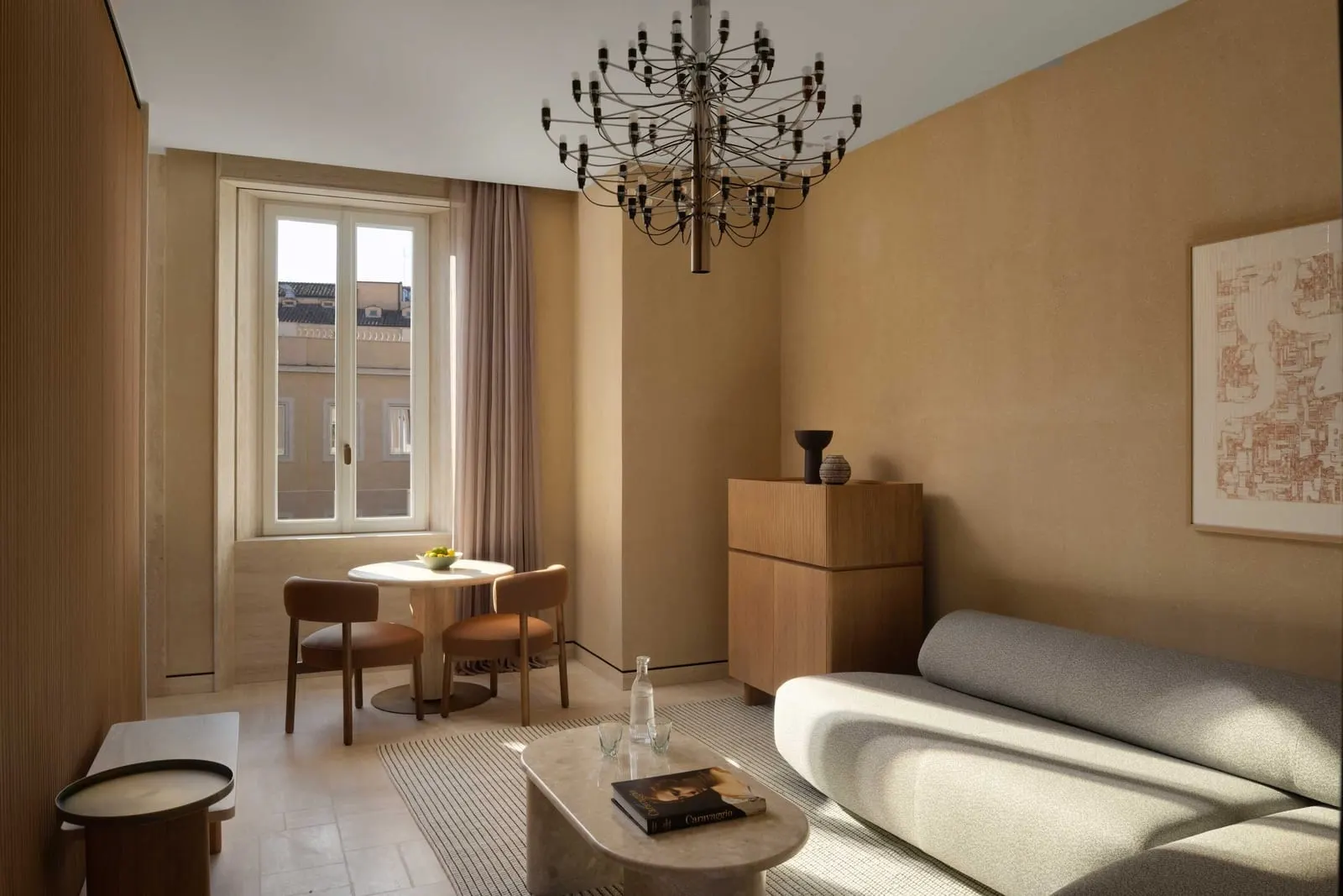 Deluxe Suite at Six Senses Rome: the living room with a curved sofa, a small dining table and a chandelier