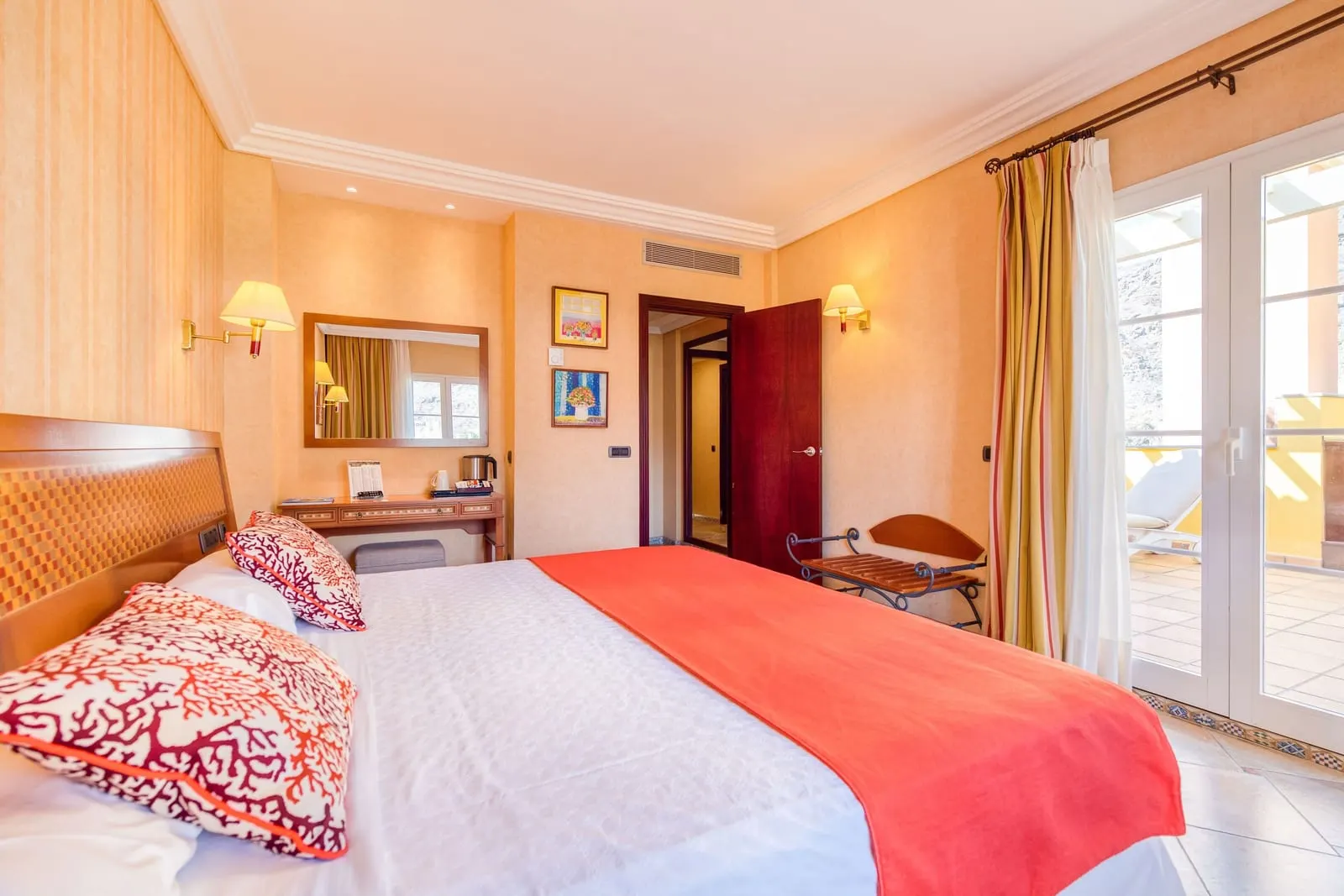 Honeymoon Room at Hotel Cordial Mogán Playa: a bed with a red throw, a dressing table with a kettle, and glass doors open to a balcony with a sunbed