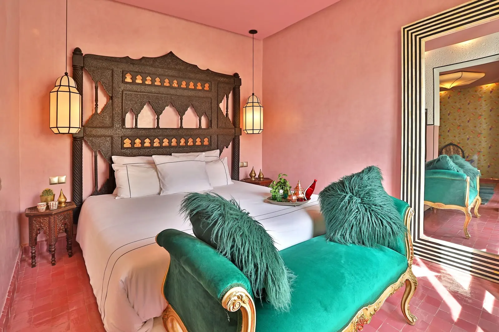 Suite De Luxe at Dar Kandi: a bed with a carved wooden headboard in a pink room, with a green velvet bench and a tall mirror