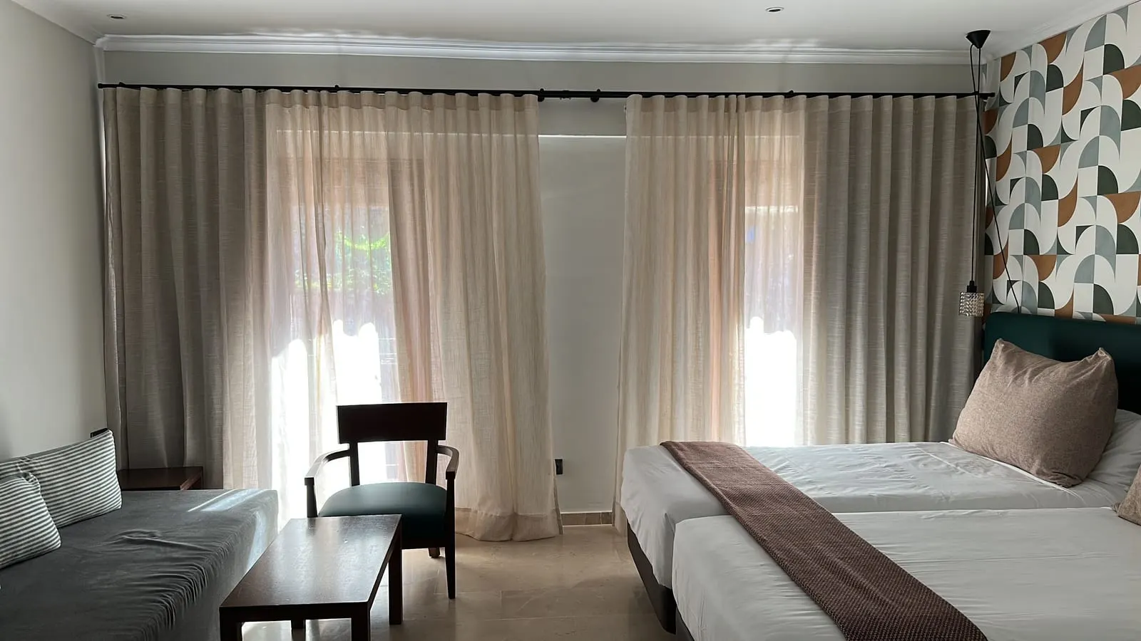 Garden Junior Suite at Maristel Hotel & Spa: twin beds beside a patterned wall, a grey sofa, a coffee table and full-height curtains