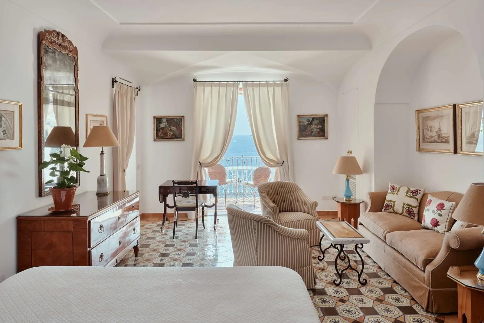 Executive Sea View at Le Sirenuse: a bed facing a sitting area with a sofa, armchairs and a writing desk, with curtained doors to the balcony
