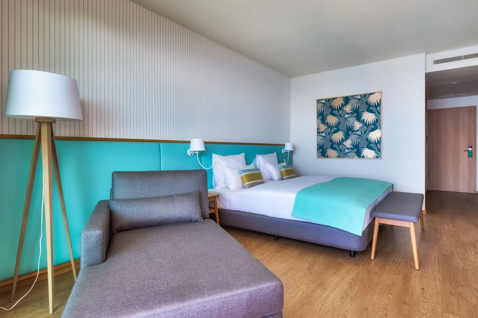 Double Room Sea View Balcony at Sentido Galomar: a made-up double bed against a turquoise headboard, a grey chaise longue, a tripod floor lamp and a leaf-print picture