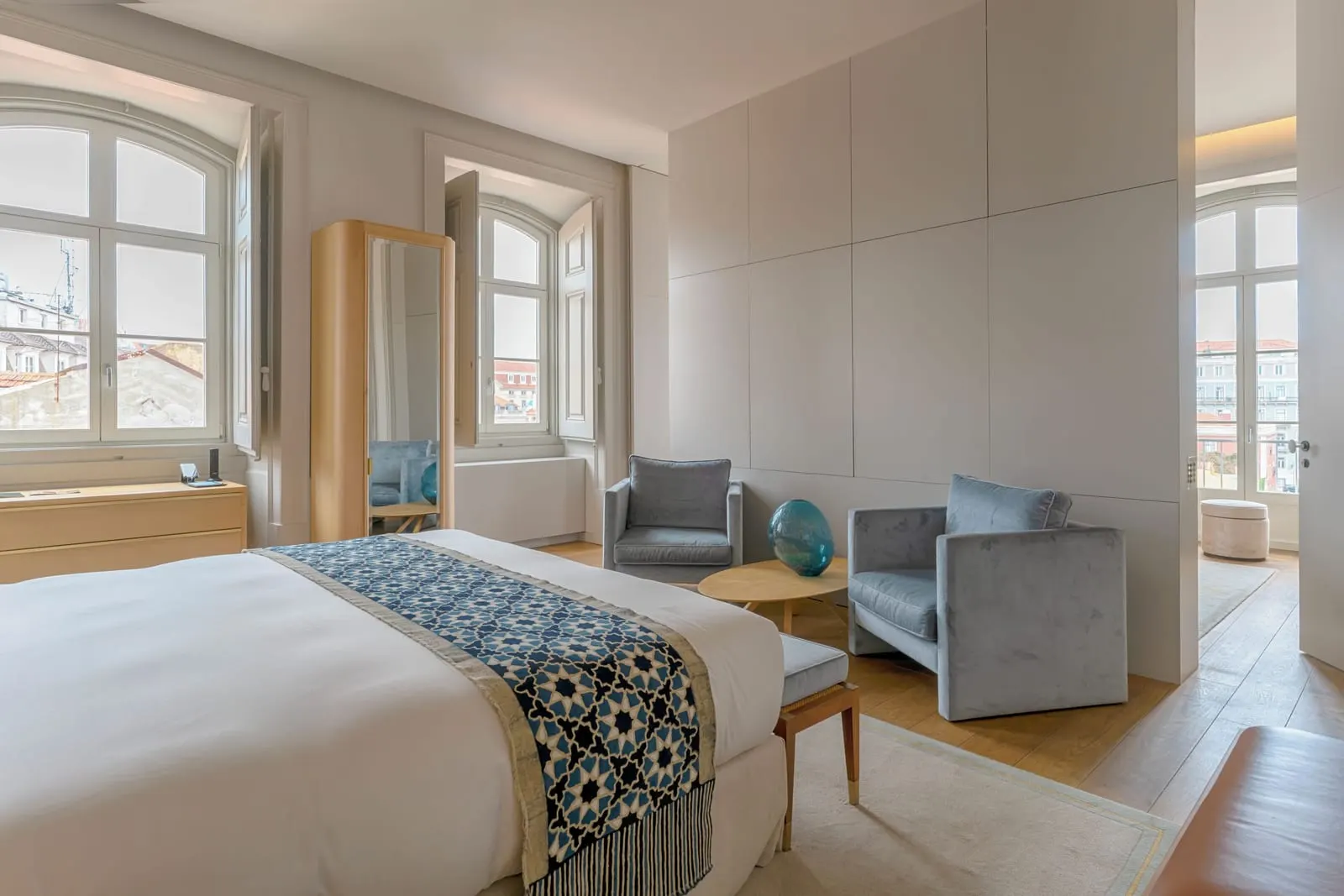 Premium Suite at Verride Palácio Santa Catarina: the bed, two grey armchairs and arched windows over the rooftops