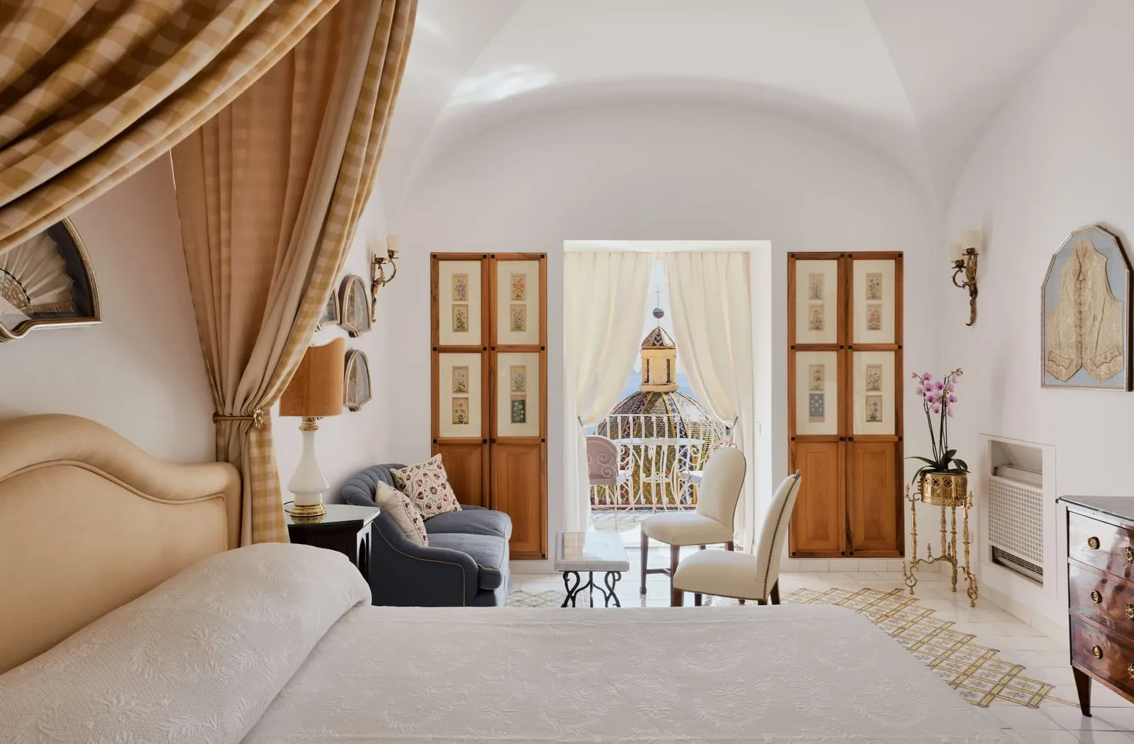 Superior Sea View at Le Sirenuse: a canopied bed and a sofa, with painted wooden shutters either side of a curtained door to the balcony