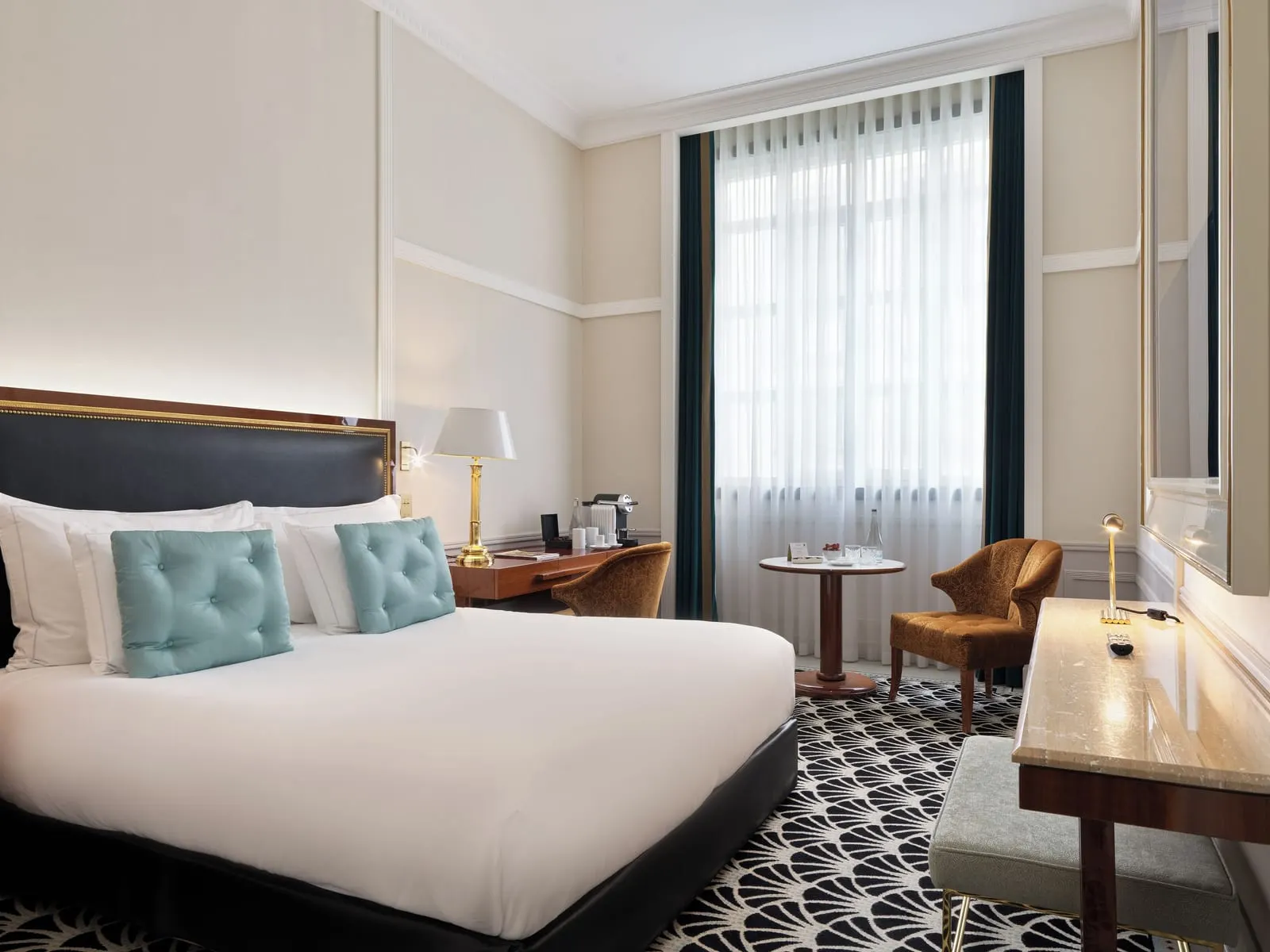Deluxe Room at The One Monumental Palace: the bed with pale blue cushions, a desk, a small round table and a tall window