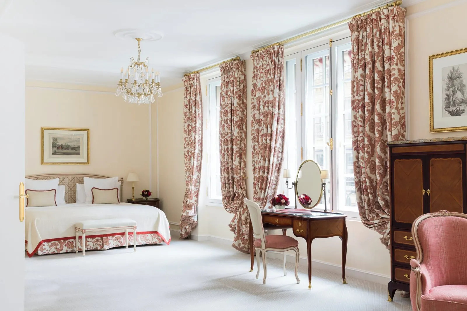 Prestige Elysée Suite at Le Bristol Paris: the bed seen from the doorway, with a dressing table and a tall wooden cabinet between windows hung with red patterned curtains