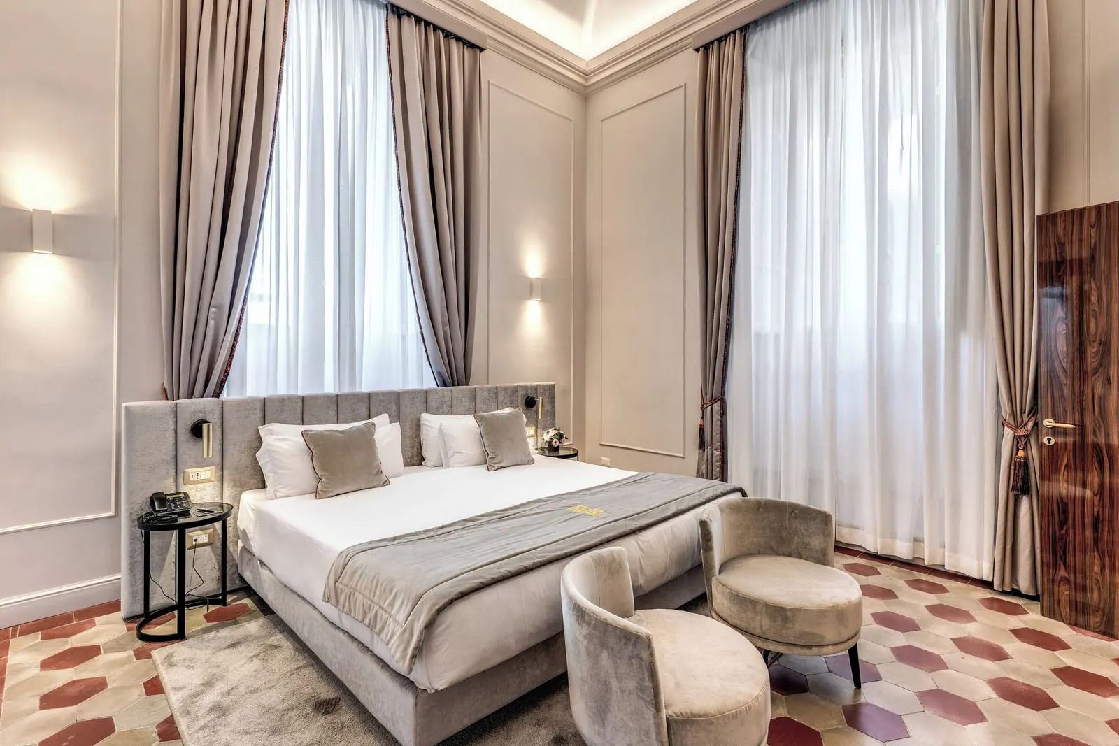 Deluxe Suite at Eitch Borromini Palazzo Pamphilj: a large bed, two armchairs and a patterned tile floor under tall curtained windows