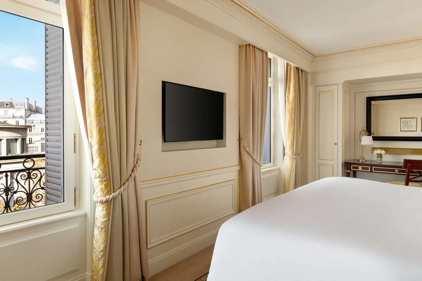 Junior Suite at Shangri-La Paris: the bedroom, with the bed, a wall-mounted television, a writing desk and a window with a wrought-iron balcony rail