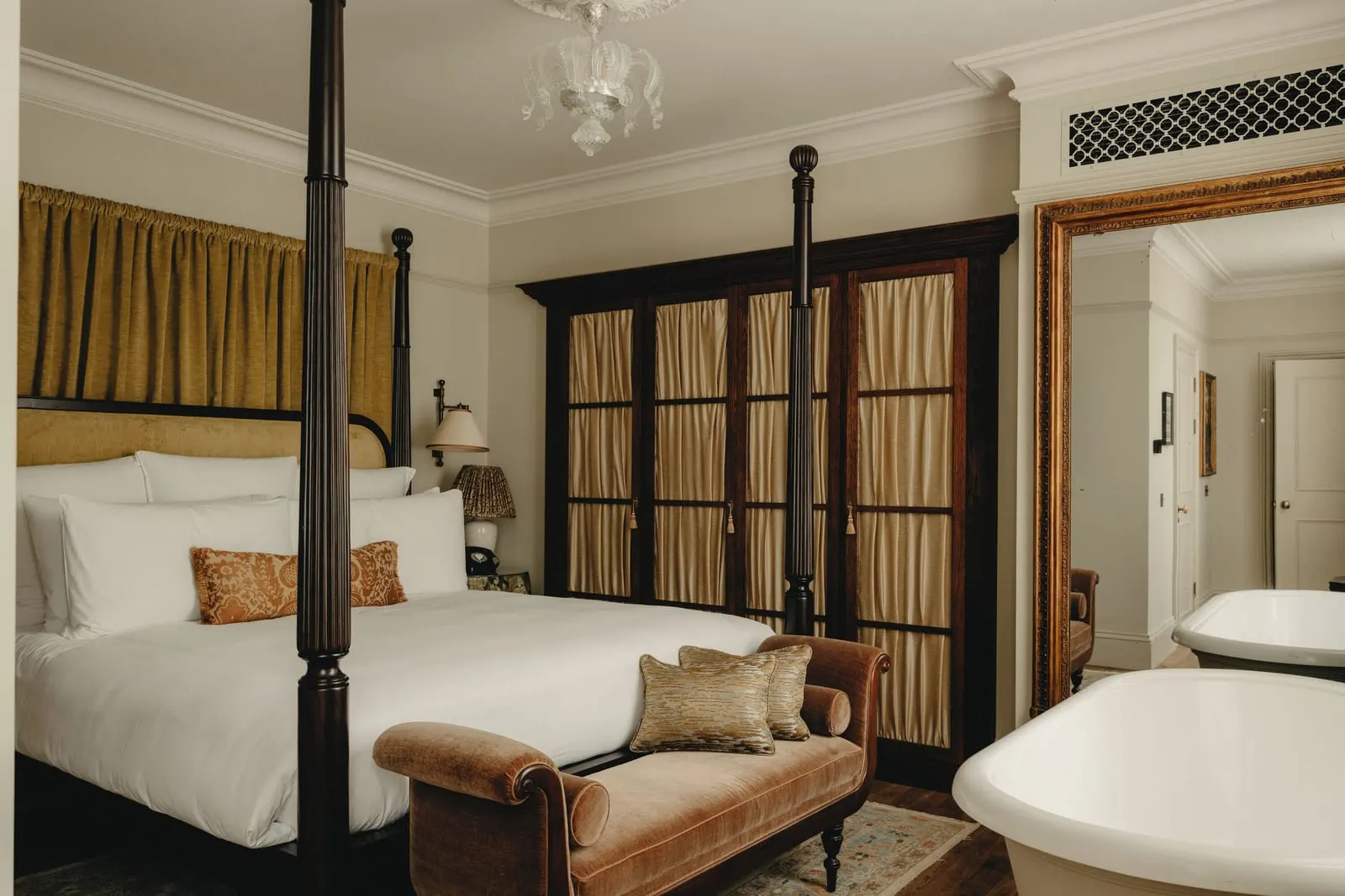 One Bed Suite at The Ned: a four-poster bed, a velvet chaise and a bath beside the bed