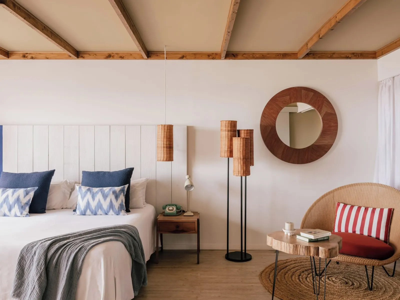Casa Zel at ZEL Fuerteventura: a double bed with blue cushions, a round wooden mirror and a wicker armchair beside a small table