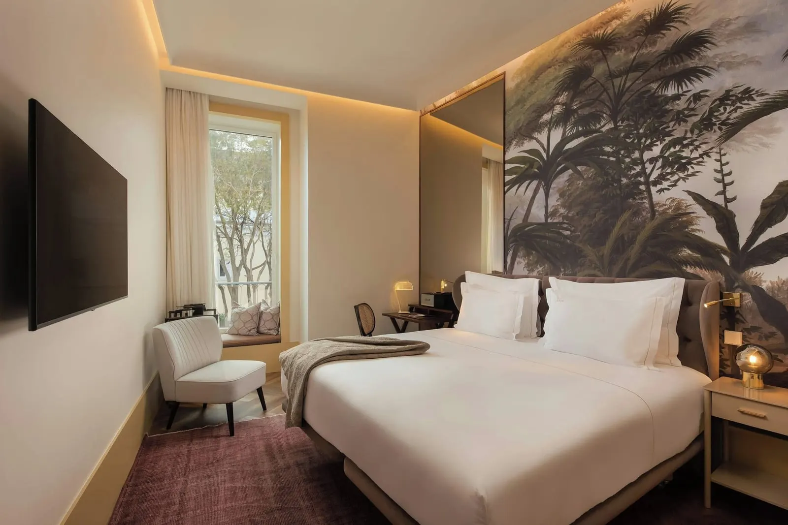 Superior room at The Ivens: the bed against a palm mural, an armchair and a tall window