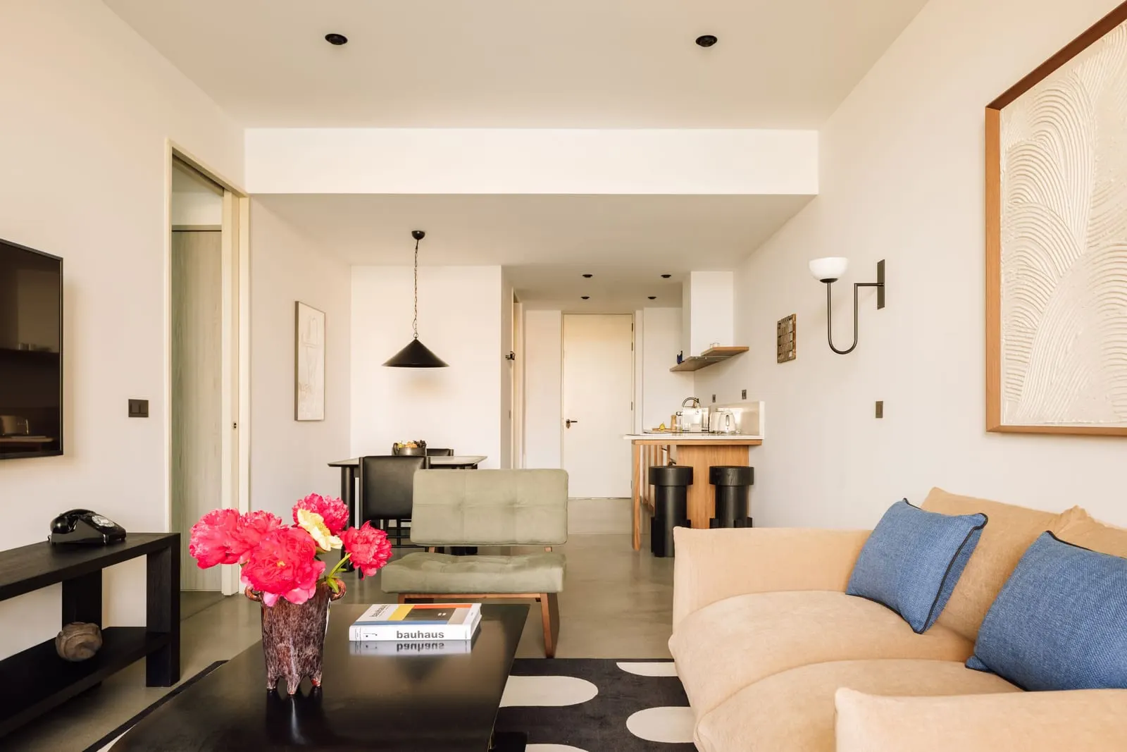 One Bedroom River Suite at The Rebello: the living room with a sofa and armchair, and the dining table and kitchen beyond